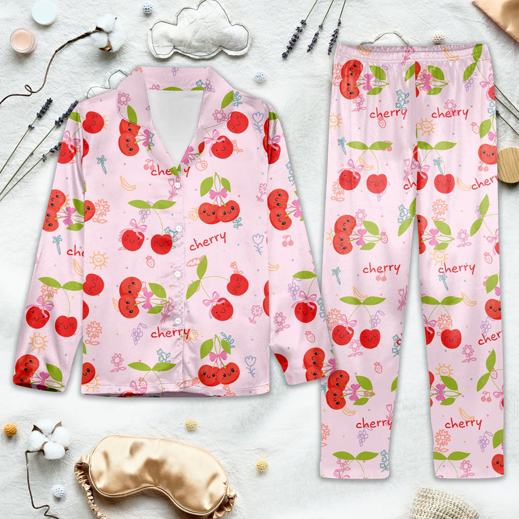 Pink pajama set with cherry pattern on a light gray surface with sleep mask and earplugs.