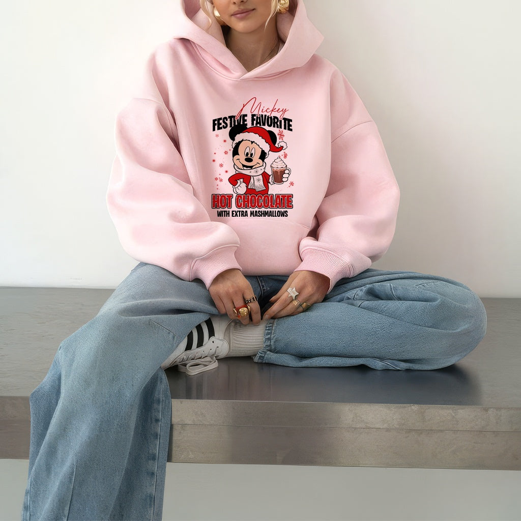 Woman wearing a pink hoodie with a festive Mickey Mouse design, sitting on a bench.