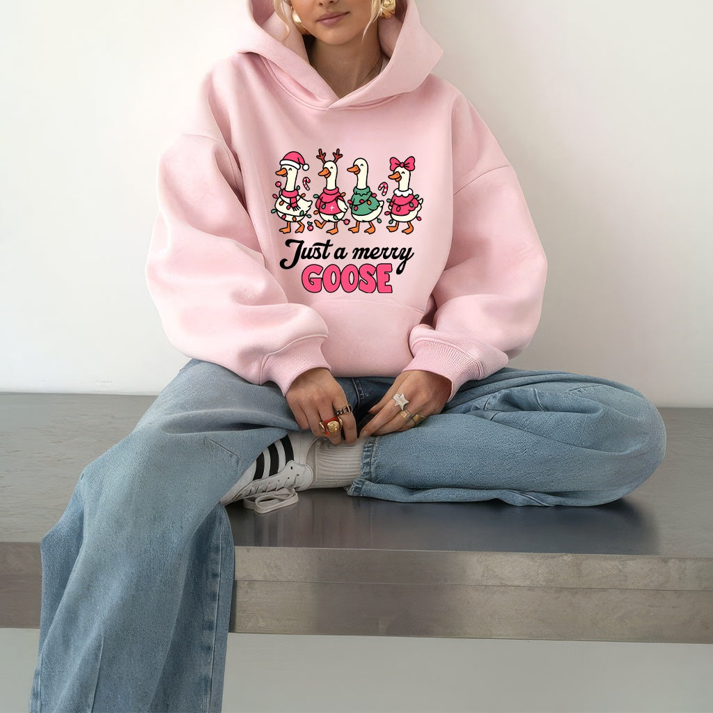 Woman wearing a pink hoodie with a Christmas-themed goose graphic design and text, sitting on a bench.