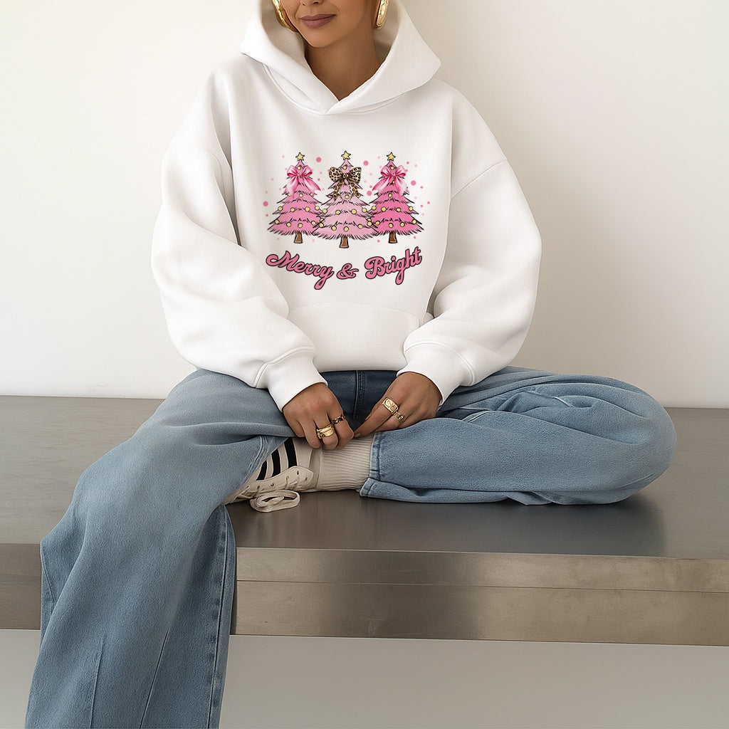 Woman wearing a white hoodie with festive Christmas Trees and text, sitting on a bench.