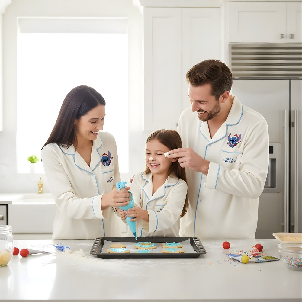 Family of three in matching beige pajama set with Stitch in a Santa Claus outfit decorating cookies in a kitchen.