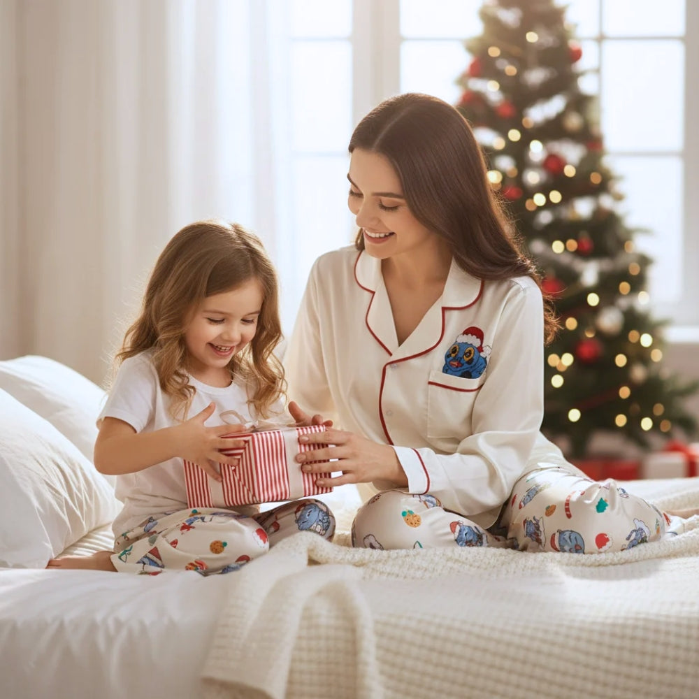 Woman and child in pajamas with colorful Derpy tiger patterns and holiday designs opening a gift on a bed with a Christmas tree in the background