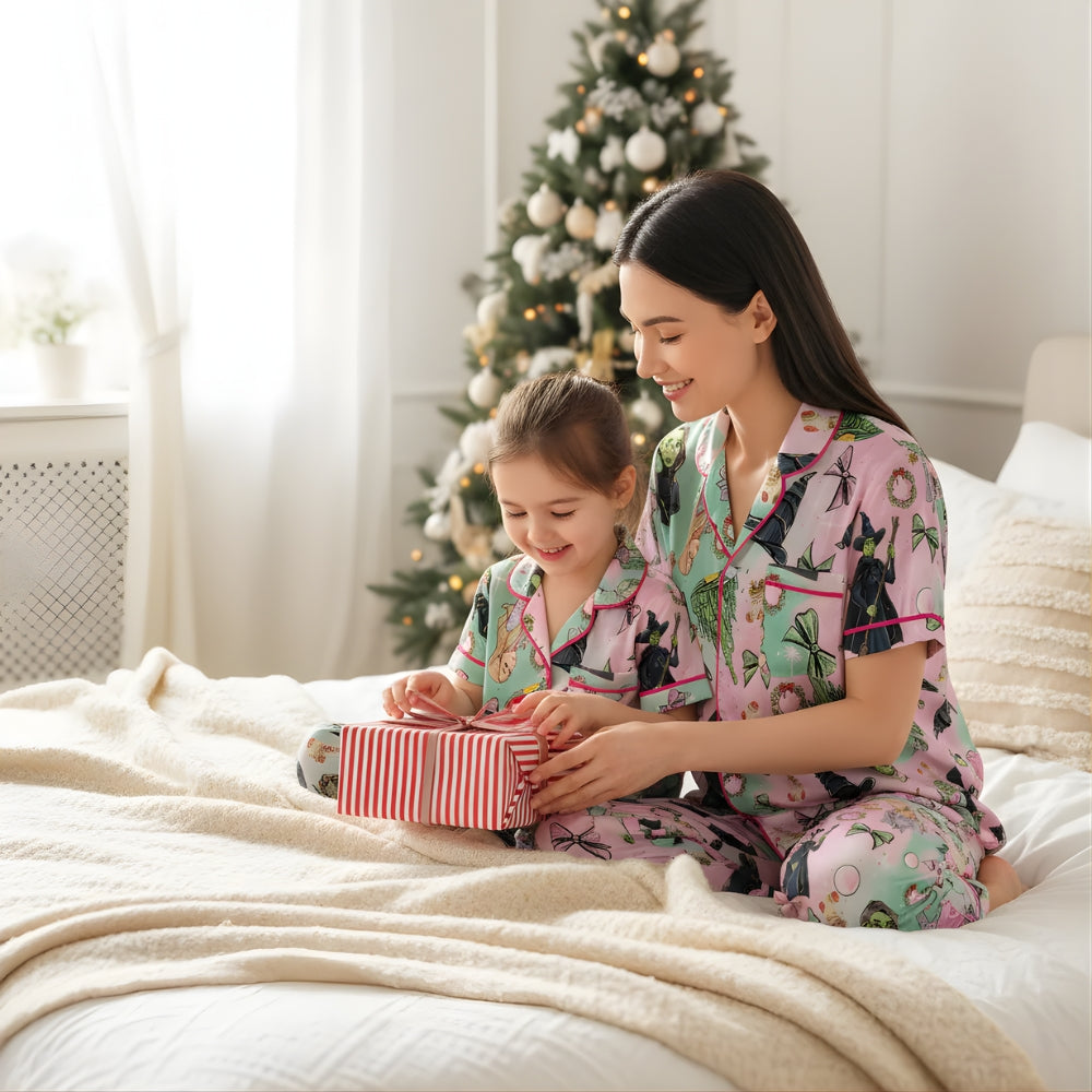 Woman and child in matching pajamas with the iconic colours of Glinda and Elphaba opening a gift in front of a Christmas tree.