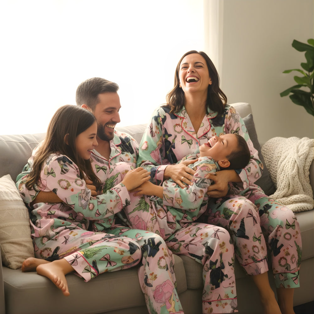 Family of four in matching pajamas with the iconic colours of Glinda and Elphaba sitting on a couch, laughing together.