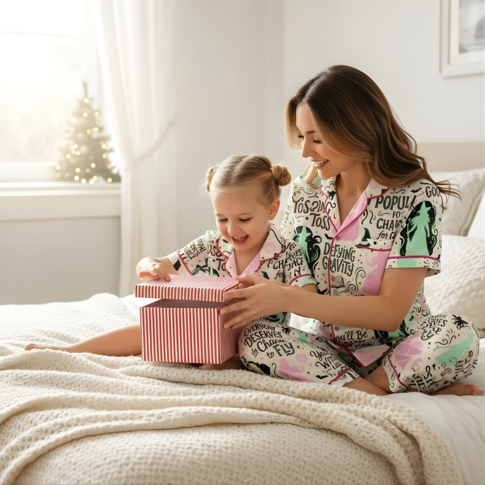 Woman and child in matching pajamas with the enchanting world of Oz design with a stylish, theatre-inspired twist opening a gift box on a bed.
