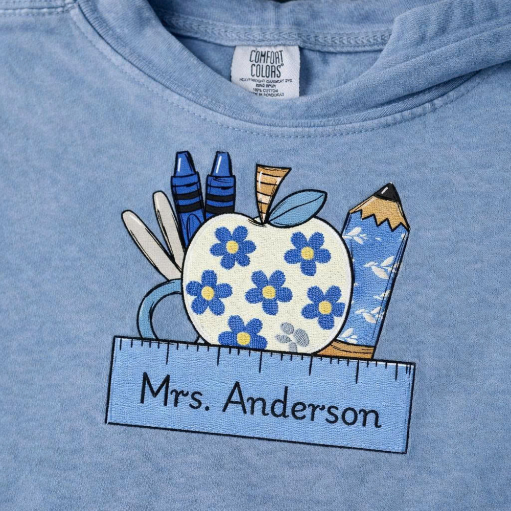Blue hoodie with a decorative design of an apple with flowers, pencils, and erasers, and 'Mrs. Anderson' text.