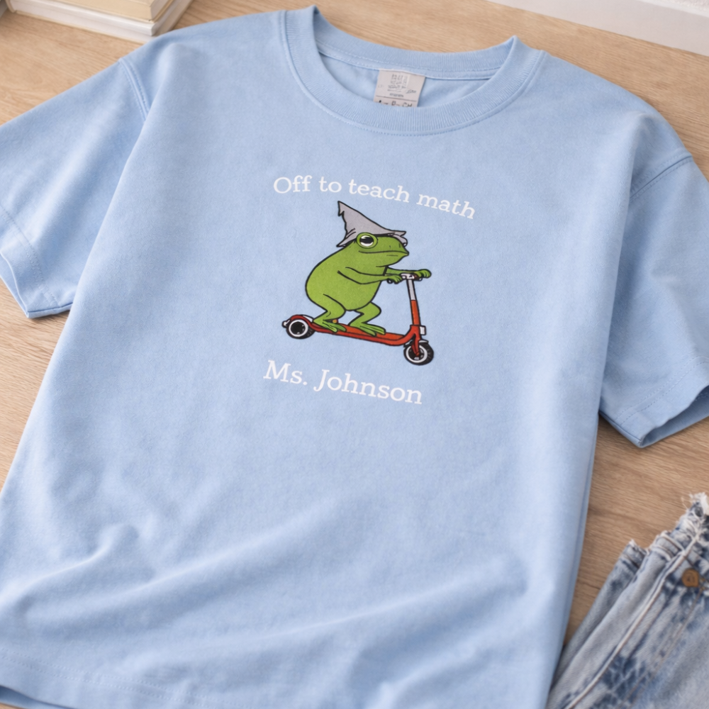 Light blue t-shirt with a frog graphic and text on a wooden surface